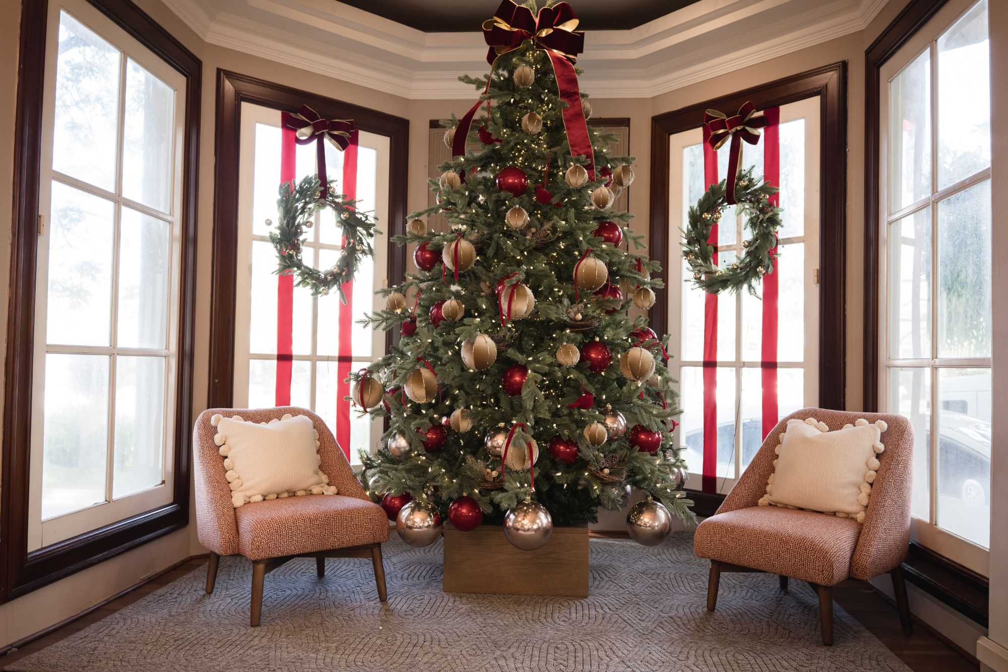 Árbol de Navidad con esferas rojas y doradas, coronas en las ventanas y dos butacas tapizadas